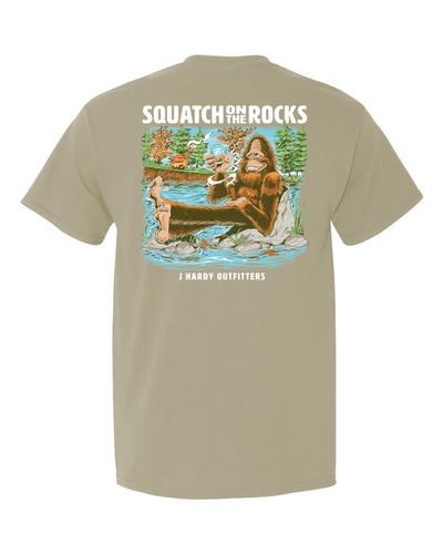 Embrace the spirit of wild relaxation with the "Sashquatch on the Rocks" t-shirt! This classic-fit tee features a humorous illustration of a mythical Sasquatch enjoying a well-deserved break. Perched on riverside rocks, he savors a glass of bourbon and a cigar – a relatable scene for anyone who appreciates the simple pleasures of unwinding in nature.